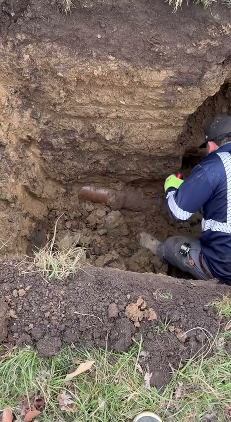 Worker repairing sewer line in deep trench